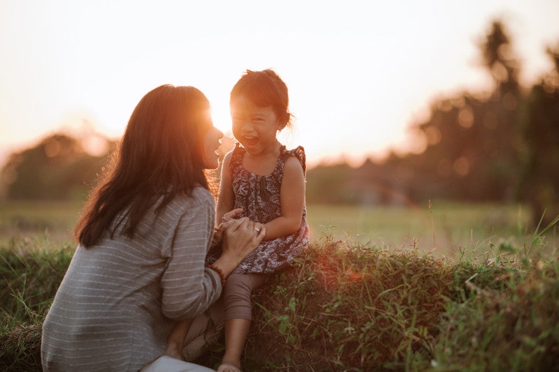 A mom holding the hands of an excited little in nature under sunset sky, knowing that connecting with nature increase gut microbiome diversity.