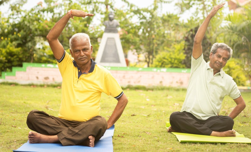 Happy senior people doing yoga by stretching hands - Concept of Senior people fitness and healthy lifestyle - two elderly man busy in morning exercise