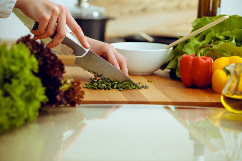 Side profile of hands chopping herbs on a cutting board surrounded by vegetables, showing that functional medicine health coaching and the elimination diet has shown positive health outcomes.