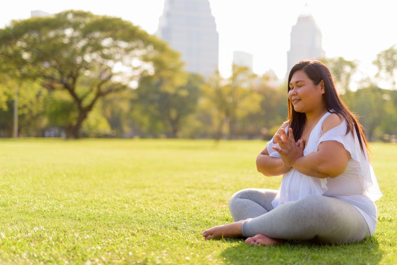 Portrait of beautiful overweight Asian woman meditating in Central Park, decreasing hyperactive mast cells by incorporating mindfulness into her life.