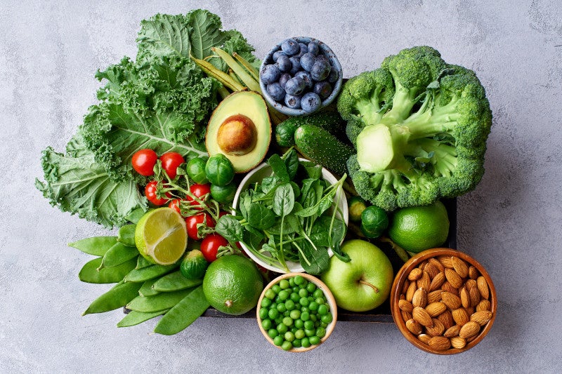 Creative flat lay with healthy vegetarian meal ingredients. Raw food concept. Broccoli, avocado, green beans, spinach, tomatoes, apples, lime and kale in wooden box on concrete background