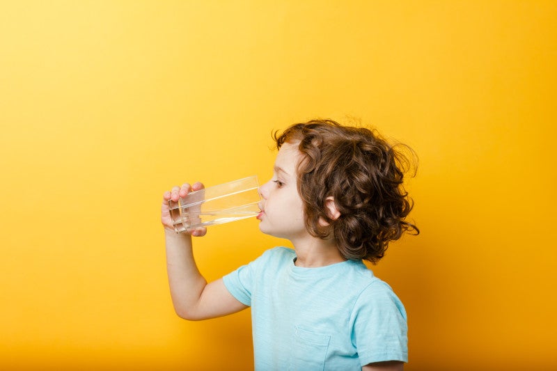 Little boy drinking clean water in front of an orange background, understanding how reducing endocrine disruptors can help lower the inflammatory burden and type 2 diabetes risk.