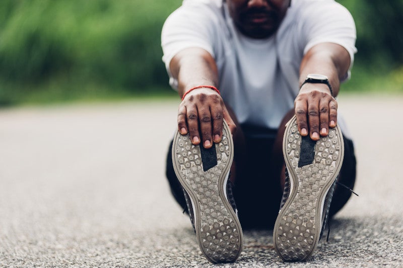 Closeup of black male sitting on the ground stretching his legs before running to help his genes and health by using lifestyle interventions, such as exercise.