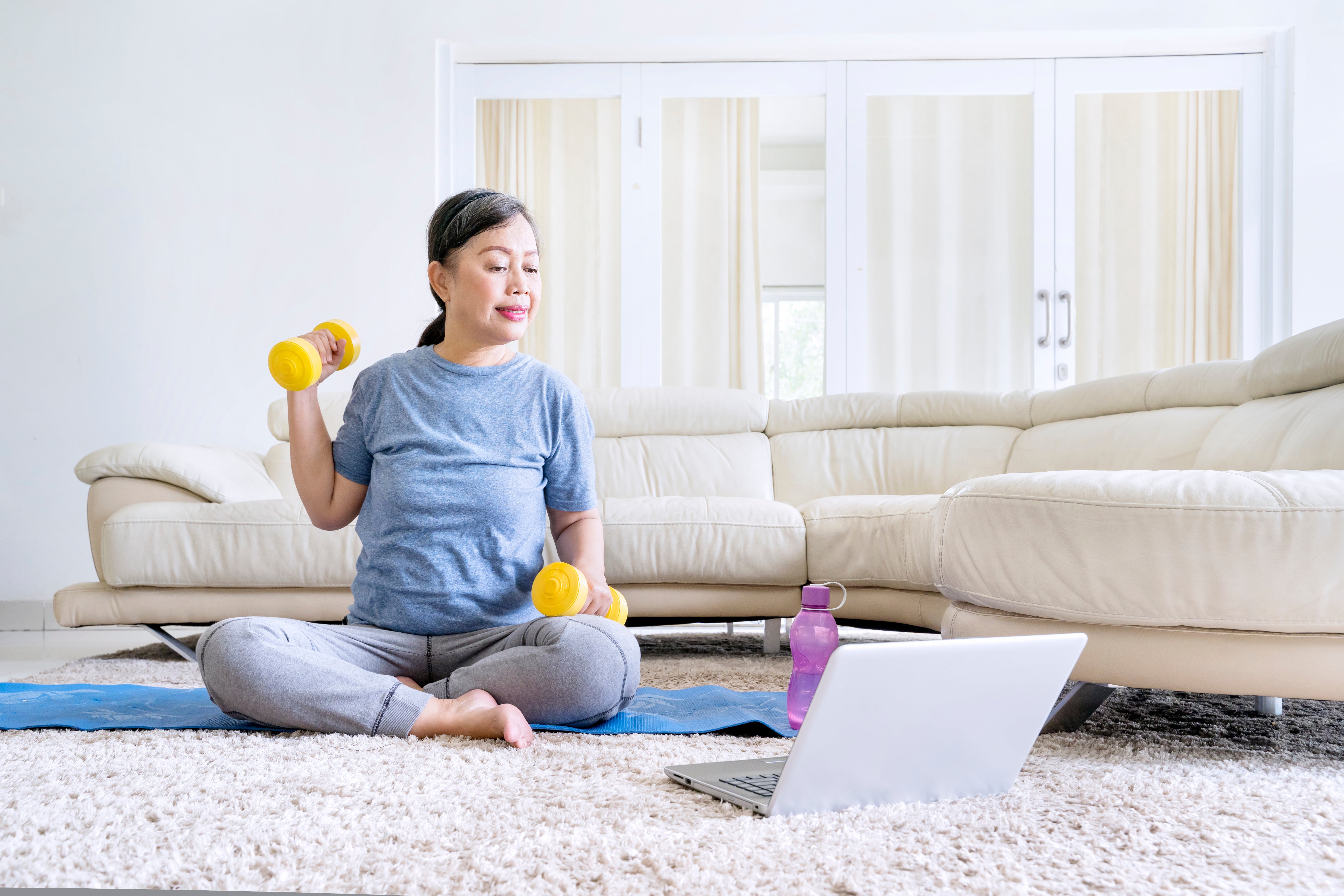 Old woman exercise with dumbbell and laptop at home