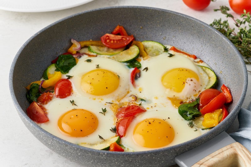 Fried eggs poached with vegetables on teflon pan - pepper, tomatoes, spinach, peppers, onion