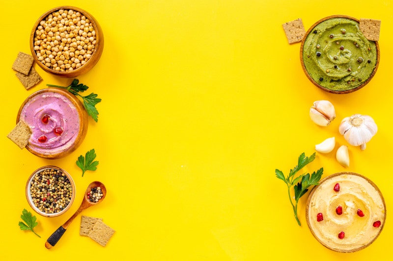 Top view of beans and hummus dips in bowls on a bright yellow background shows that nutrition interventions may be beneficial treatments for depression and mental health disorders.