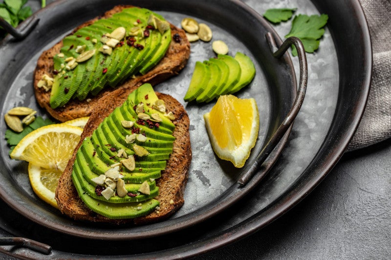 Avocado toasts with rye bread, pumpkin seeds, salt and pepper in a cast iron pan, showing that eating less ultra processed foods helps lower Alzheimer risk.