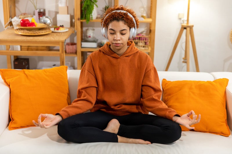 Young Black girl meditating on her couch with headphones on, a functional medicine therapy which helps her cortisol curves balance.