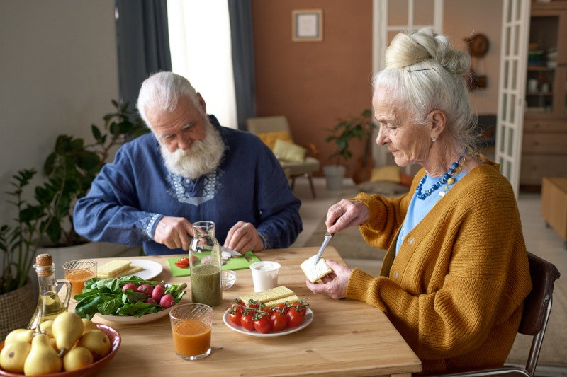 Una pareja de ancianos tomando juntos un desayuno rico en nutrientes, apoyando su microbioma intestinal y aliviando el dolor autoinmune.