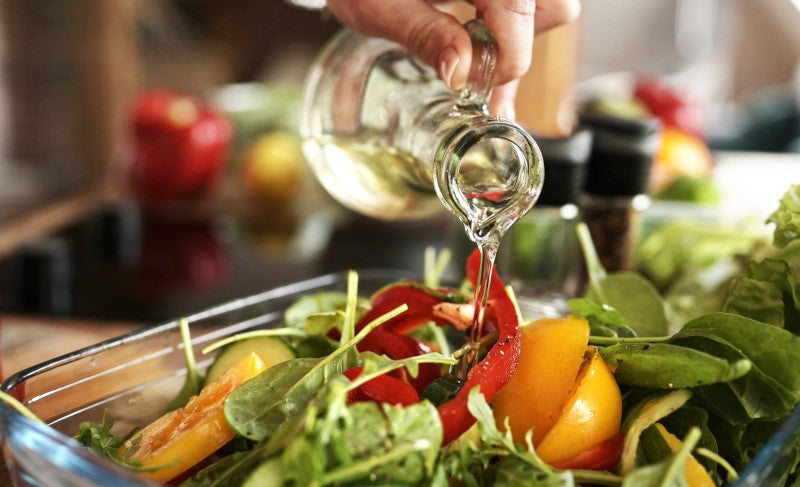 Close up of a hand pouring olive oil on a colorful salad that has essential nutrition for women's health and menopause.
