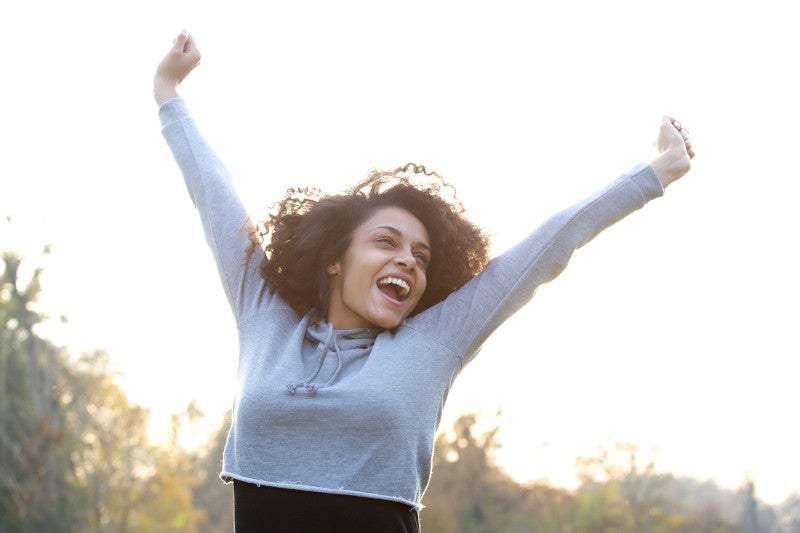 Carefree young woman smiling with arms raised