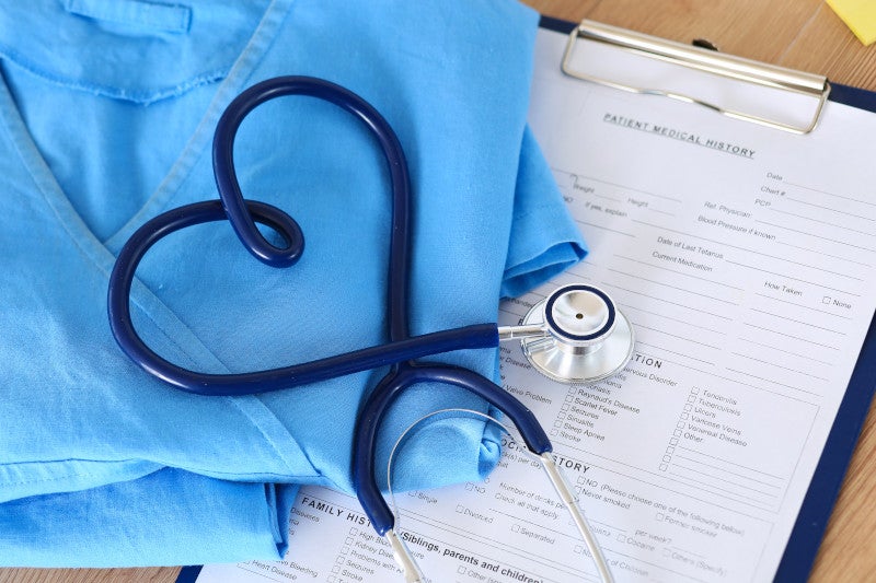 Medical stethoscope twisted in heart shape lying on patient medical history list and blue doctor uniform closeup. Medical help or insurance concept. Cardiology care, health, protection and prevention