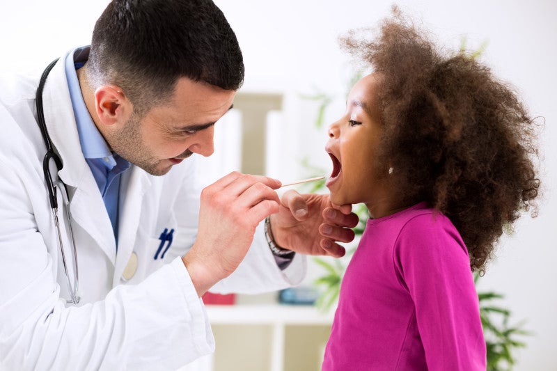 Pediatrician examining cute smiling childs throat