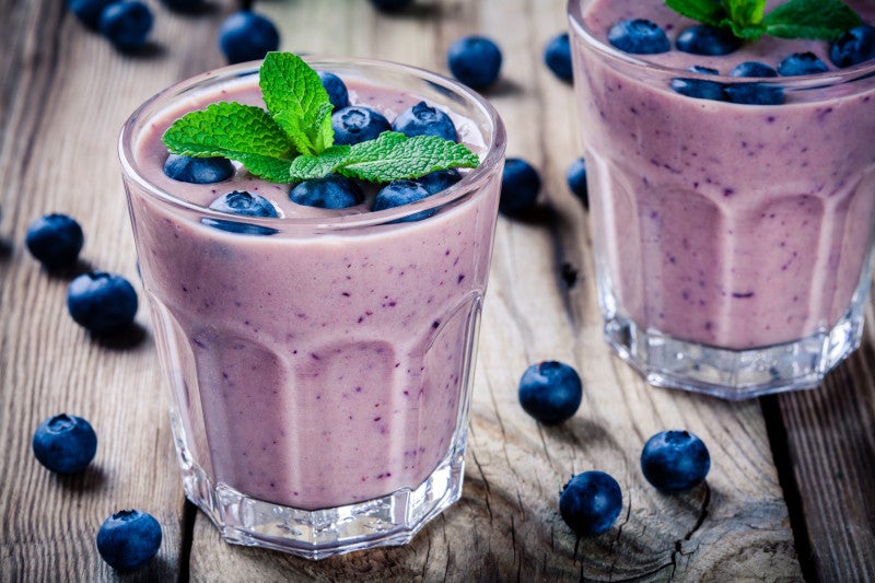 Two blueberry smoothies on a wooden table scattered with blueberries, choosing healthy nutrition to combat neurodegenerative disease.