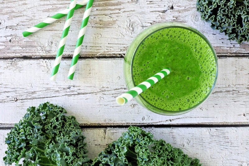 green kale smoothie overhead view in a glass with straw on an aged wood background