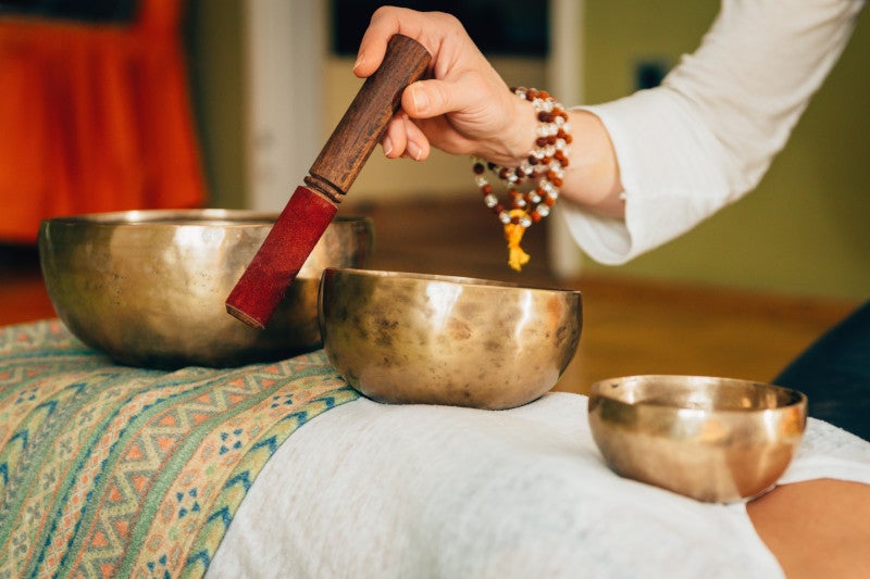 Person ringing a Tibetan singing bowl as a spirituality and stress coping mechanism for improving cardiovascular health and general quality of life benefits.