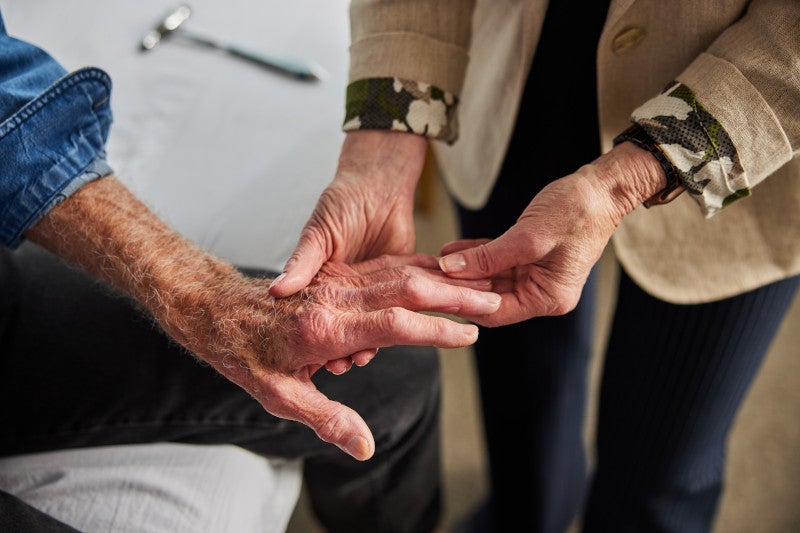 Doctor holding and assessing the hand of a patient, explaining the early onset triggers of rheumatoid arthritis and how functional medicine can help slow disease progression.