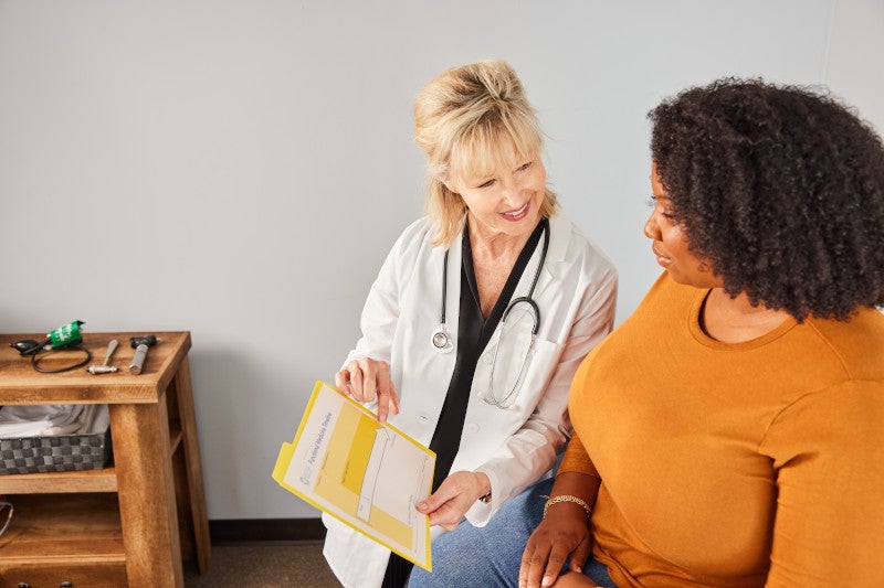 Smiling doctor showing a chart to a patient, helping to facilitate a higher health outcome by building a strong, collaborative relationship with her patient.