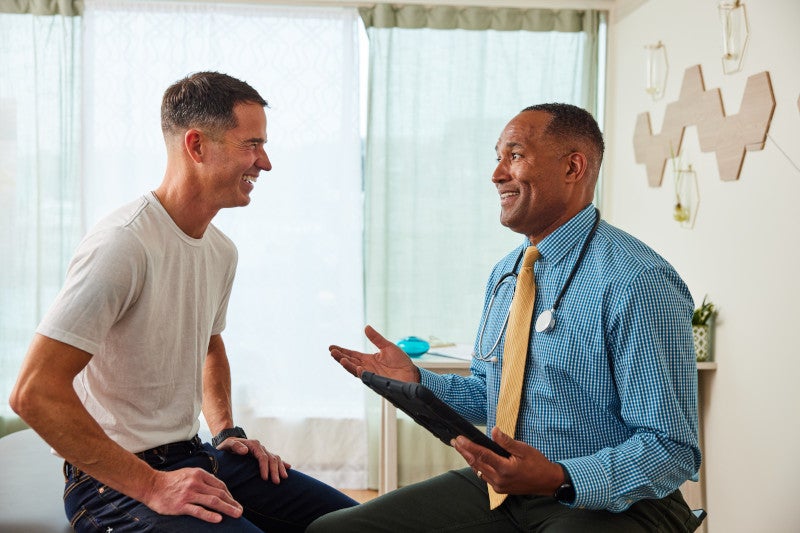 A male functional medicine doctor sitting in an office with a patient talking to him about health coaching to help wmpower him on his healing journey.
