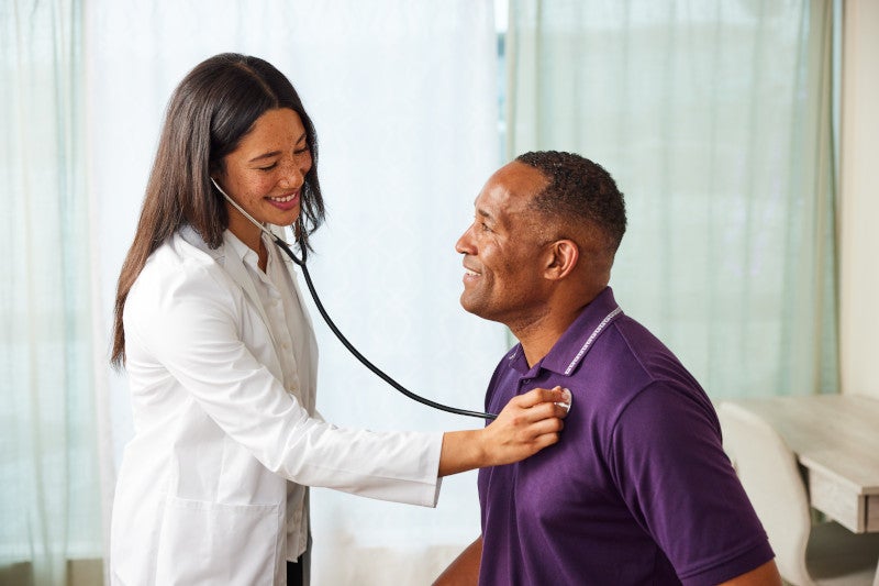 Women doctor holding stethoscope to the chest of a male patient and speaking to him about how functional medicine may help reduce his asthma.