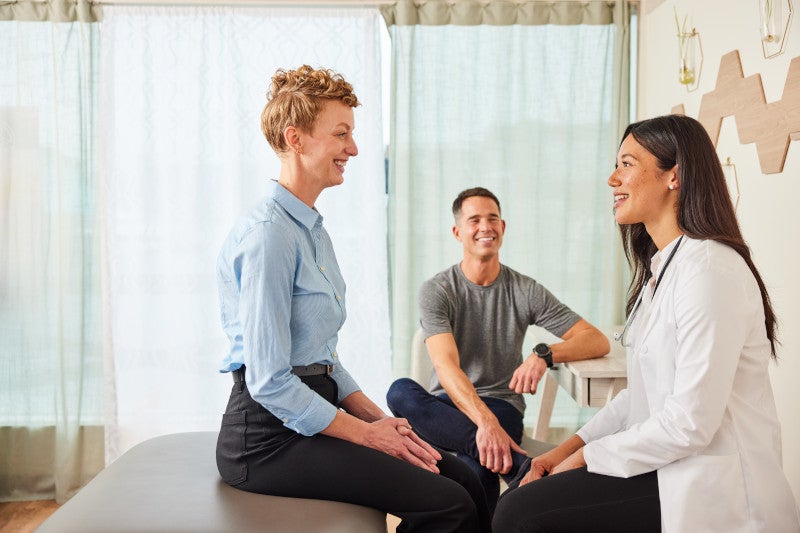 A functional medicine doctor sitting with her patient and her husband in a doctors office, offering her functional medicine solutions for her chronic pain.