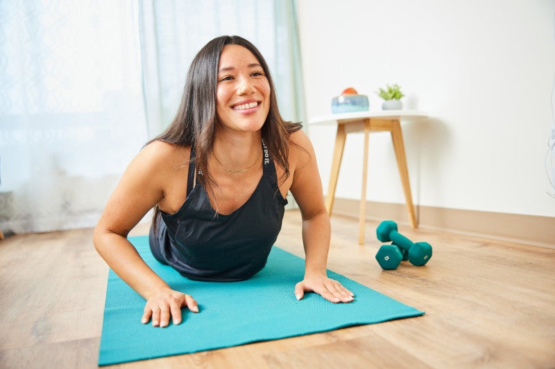 Young smiling woman in a yoga pose, using yoga as a way to reduce her PCOS symptoms.