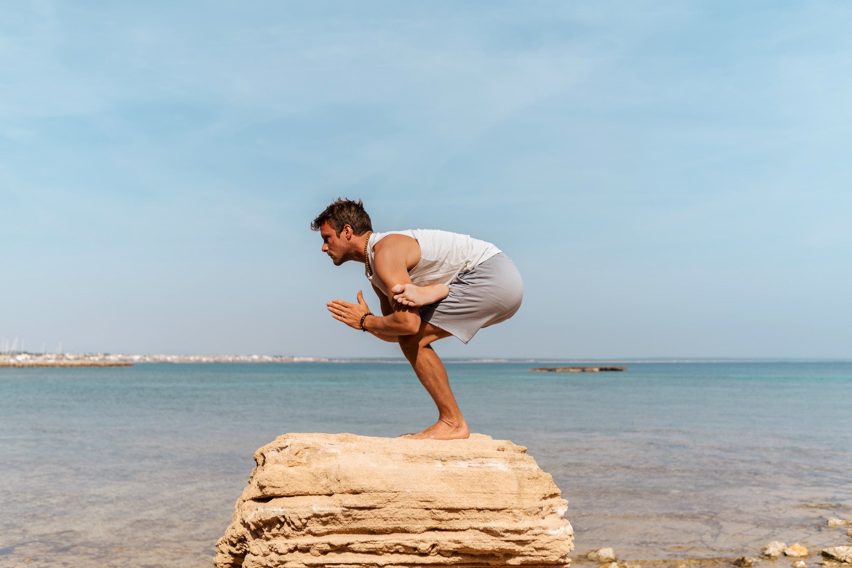 Man practicing a one leg balance pose on top of a rock by the ocean. Yoga stimulates the vagal nerve and may reduce PTSD symptoms.