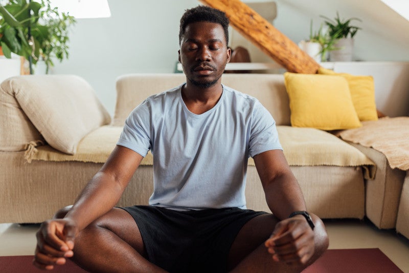 African american man relaxing doing meditation in his living room.