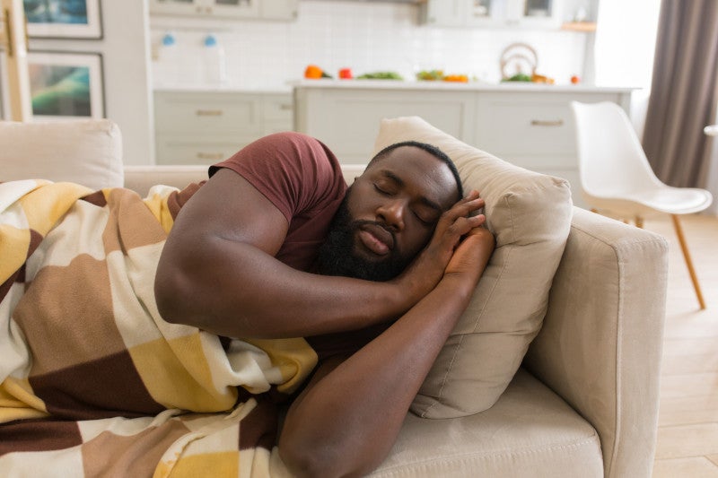 African American man sleeping wrapped in a blanket, kitchen in the background