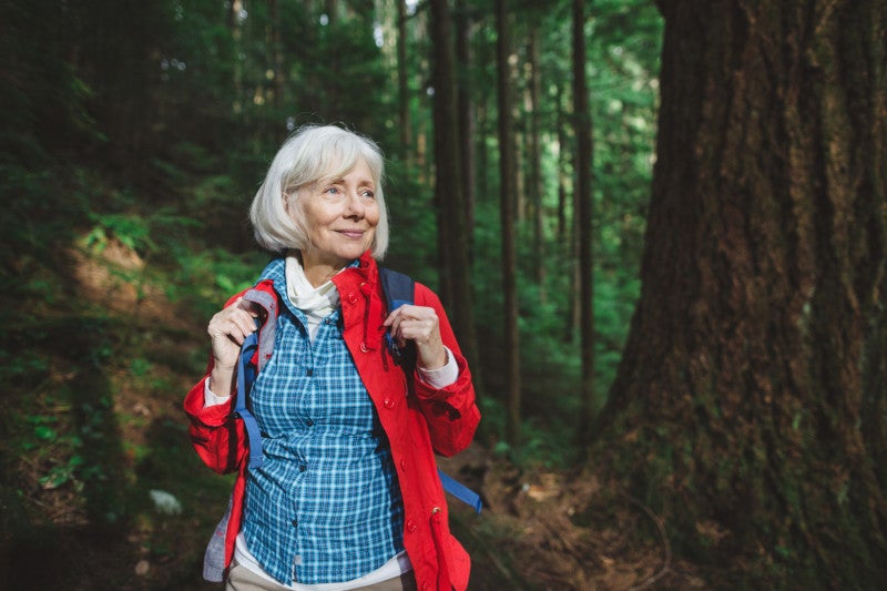 Cheerful elderly woman hiking in the forest and using physical exercise and nature as a hormone therapy to reduce menopause health risks.